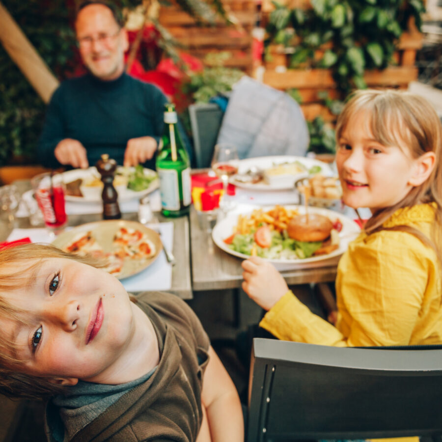 Happy family eating hamburger with french fries and pizza at outdoor restaurant in town center.