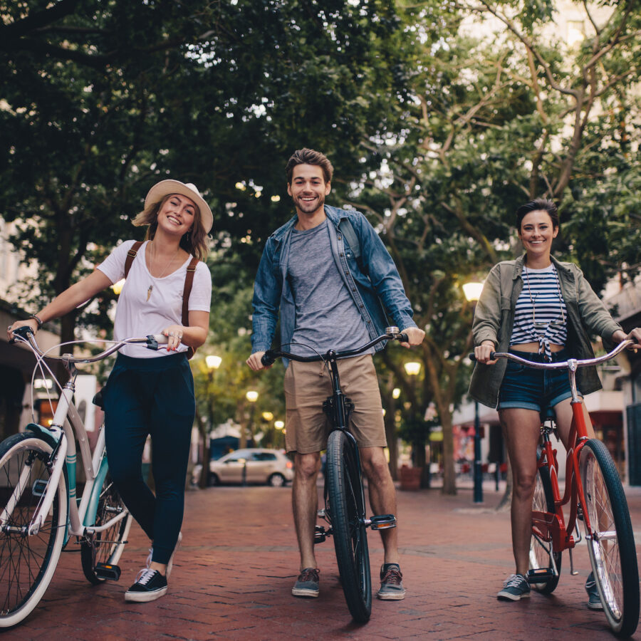 Full length of three young people with their bicycles on city street. Friends on bike ride through the town center.