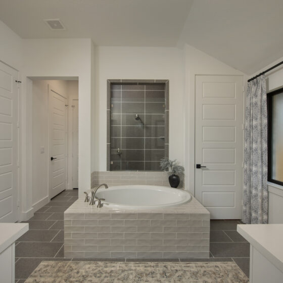 A standalone bathtub featured in the Master Bath of a Perry Home, a neutral warm white palette and tiled details