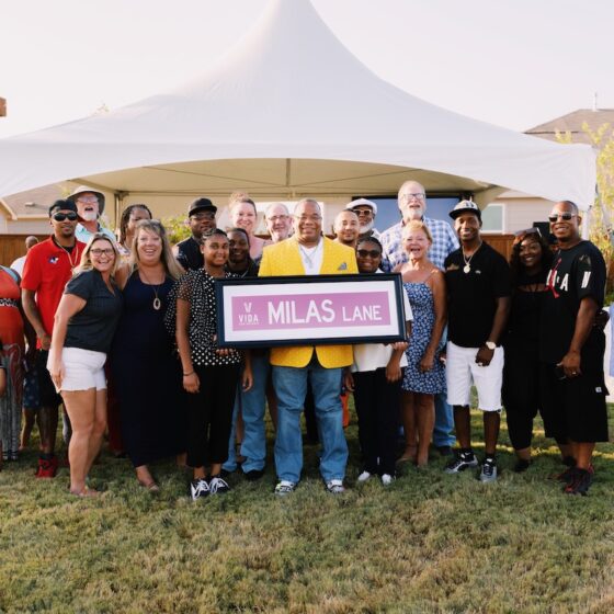 Chef Milas and community members pose for a group photo at sunset outside while he holds a sign that says "Milas Lane"