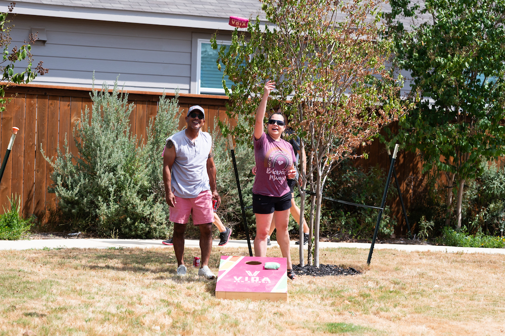 Two adults play cornhole in the sunshine at a park