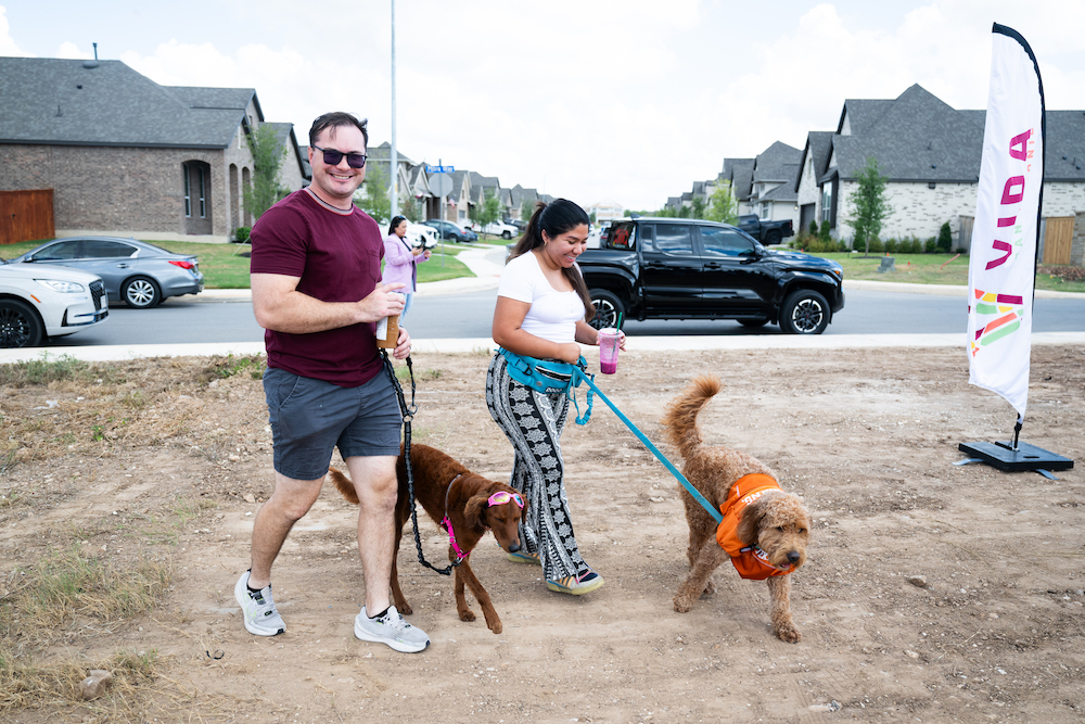 A young couple walks their dogs on leashes in a neighborhood