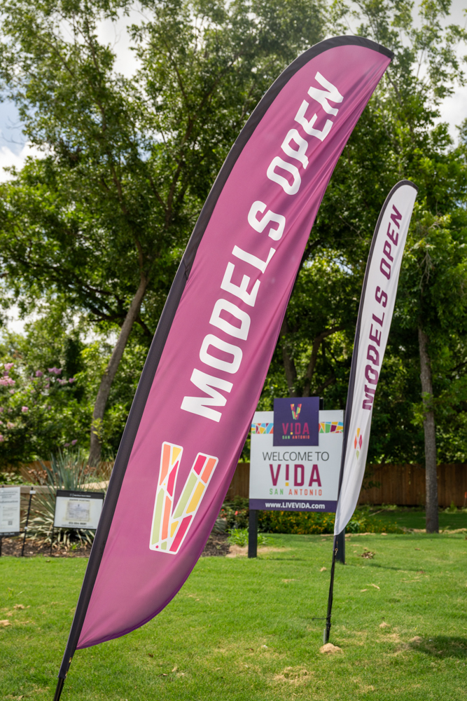 Model home open flags planted in a lawn with a "Welcome to VIDA" sign in the background.