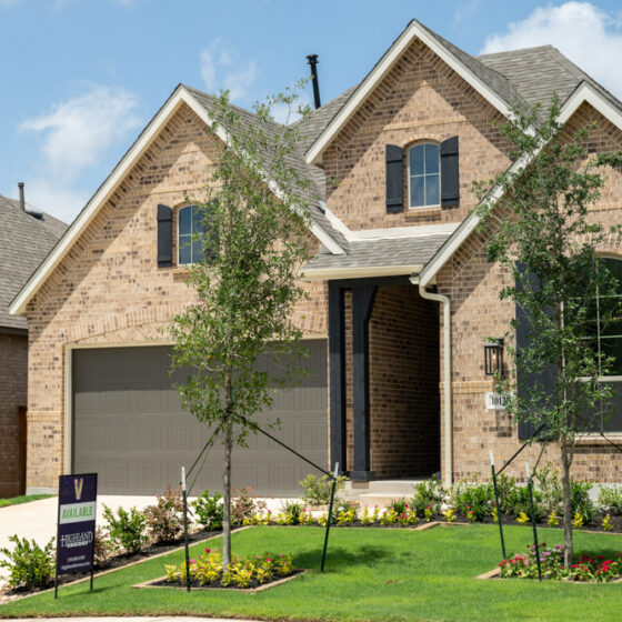 A newly constructed Highland Home for sale with brick walls, a lush front yard, young trees, and flowers