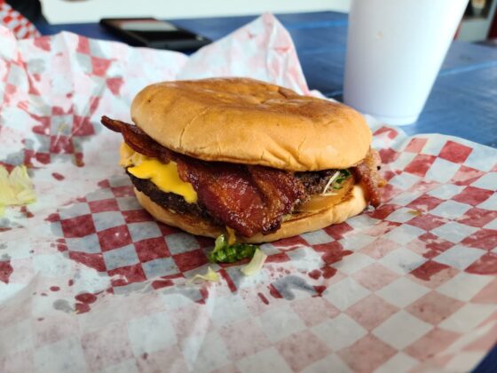 A humble burger with bacon and cheese on a red and white checkered parchment paper.