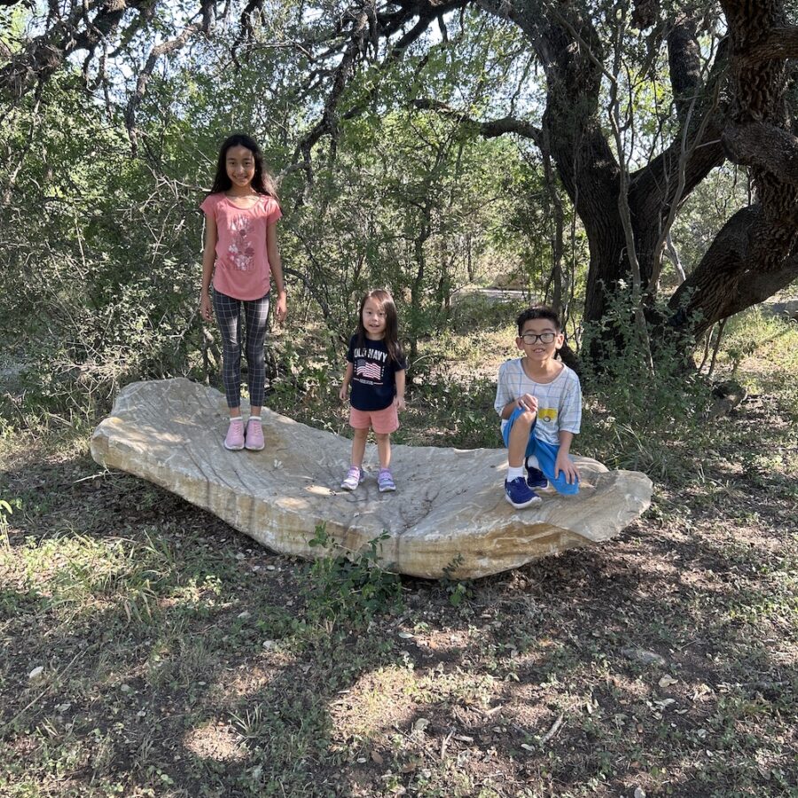 Three kids climb a large boulder and take three different poses for a photo.