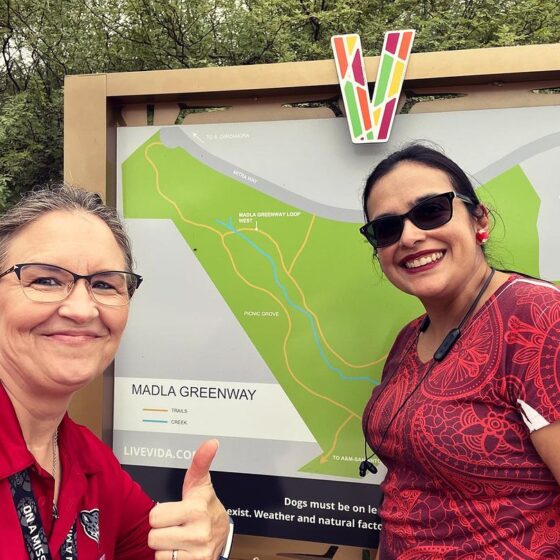 Two Texas A&M University professors take a selfie at the Madla Greenway sign