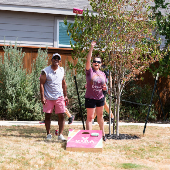 Two adults play cornhole in the sunshine at a park