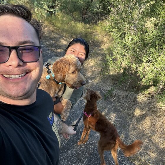 A couple and their playful dogs go for a walk on the Madla Greenway. The dogs jump up and the couple takes a fun selfie.