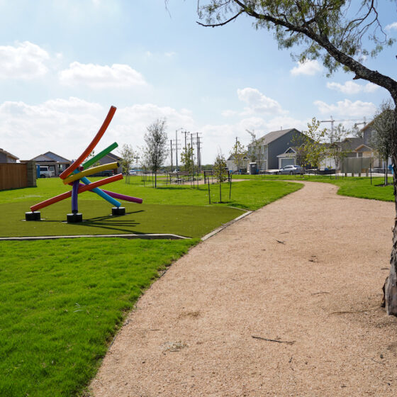 A vibrant piece of public art in San Antonio, this colorful outdoor sculpture features large, intersecting tubes in various bright colors. It stands in a park with a green lawn and a tall tree.