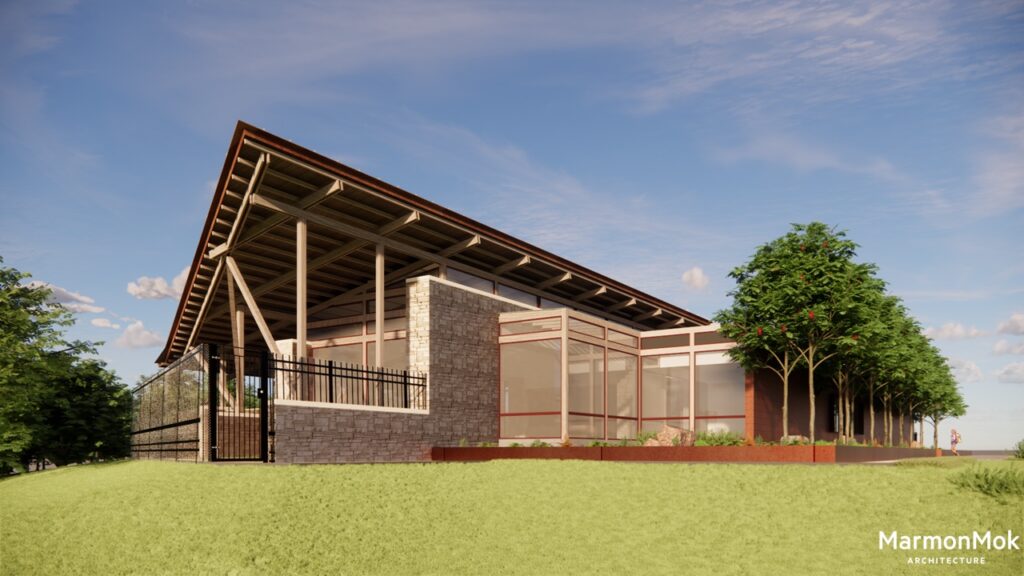 Modern building with a slanted roof and glass walls, nestled in the lush Southside San Antonio community. The design boasts stone and metal elements, complemented by a fenced area near the clubhouse. Trees add greenery around the area while a clear blue sky enhances its charm.