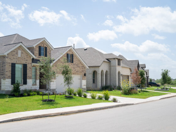 A view from the sidewalk of newly built homes with brick, puffy white clouds in the sky