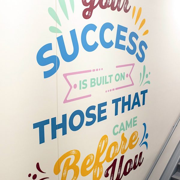 A colorful mural with fun fonts inside a school reads "Your Success is Built on Those that Came Before You"