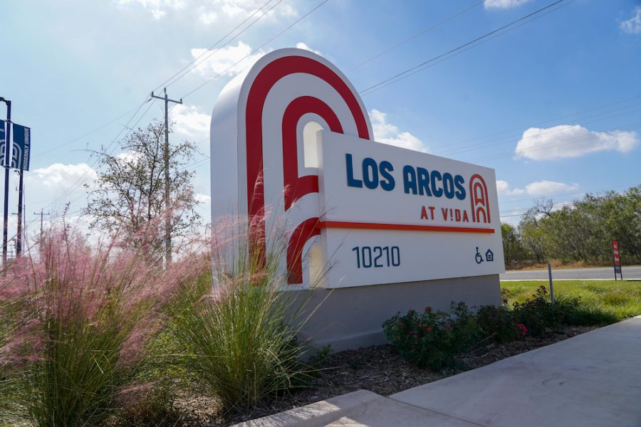 Sun shines down on an apartment community entry sign that says Los Arcos