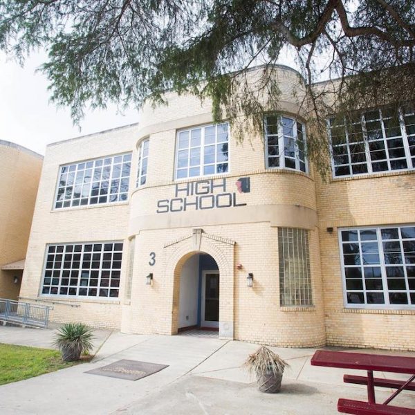 An entrance to a charter school in a two-story, sandy brick building with glass windows, trees nearby.