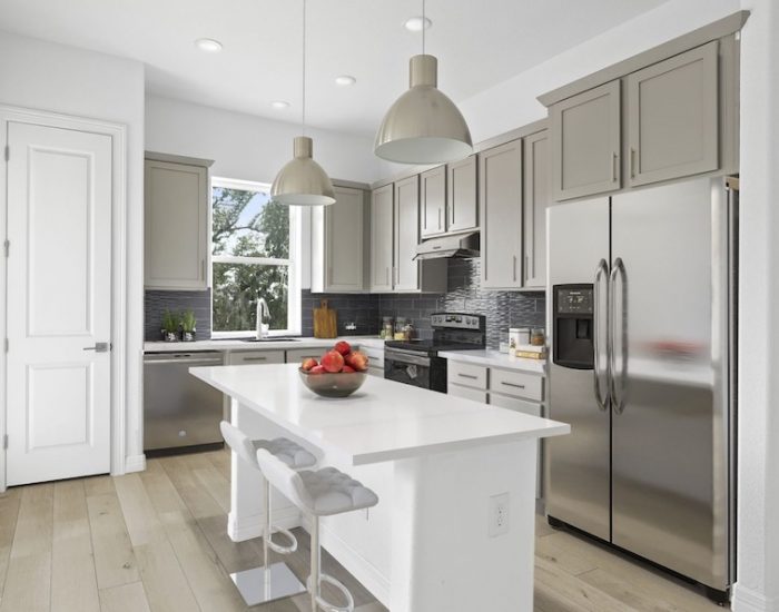 An ultra-sleek townhome kitchen with an island and a silver fridge.