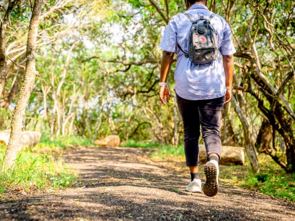 A student with a backpack and sneakers walks along the path of the Madla Greenway with dappled light amidst the trees.